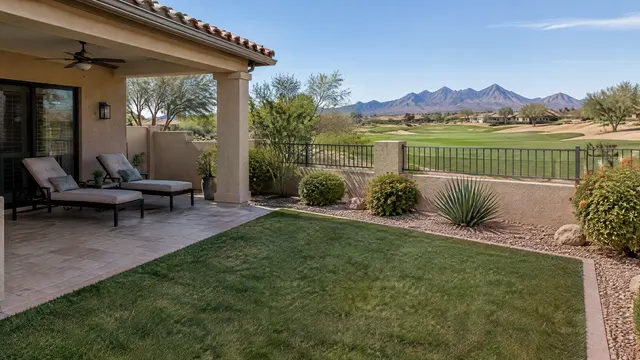 Backyard of a single-story Spanish-style home in a gated 55-plus community in south Chandler, Arizona: compact artificial turf lawn beside a covered patio with two lounge chairs, view to a golf course and the San Tan Mountains far away