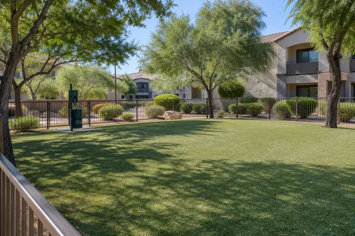 Artificial turf dog park area at an apartment community, low fence, waste station without signage, shade trees