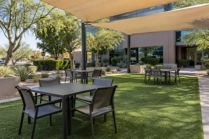 Artificial turf patio area with outdoor tables at an office building courtyard, shade canopy overhead