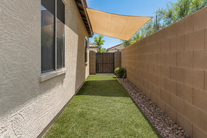 Narrow dog run along the side of a Chandler home with artificial turf, a shade sail, a gate and a gravel border