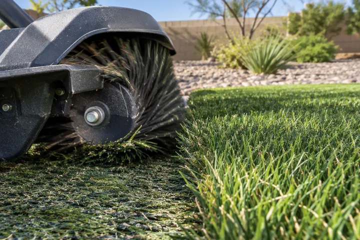 Close-up of artificial turf blades being lifted by a rotating power brush, matted section next to a fluffed section